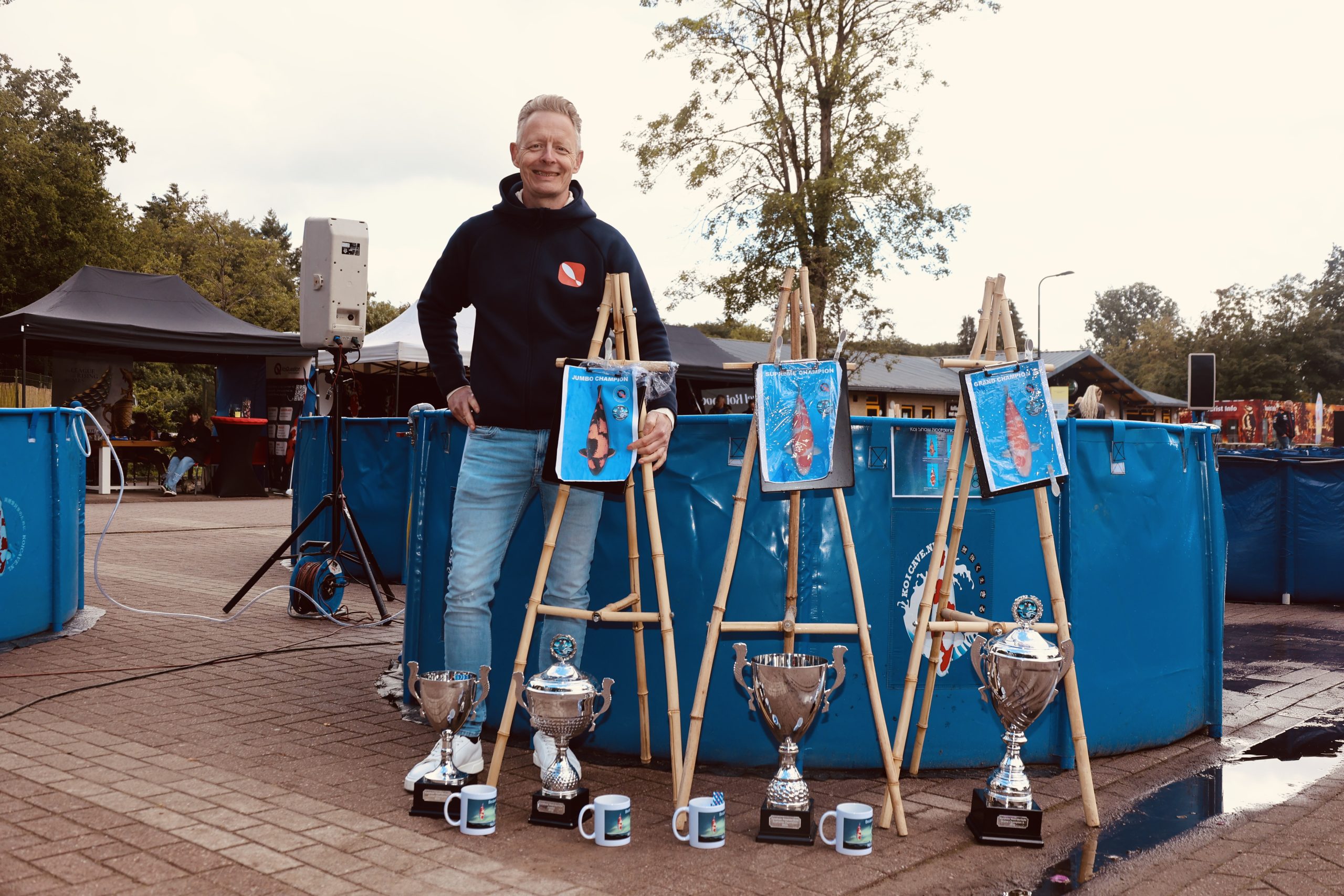 Geert Schrijvers tampak bangga berdiri di samping ikan Koi pemenang hadiahnya, yang dilengkapi dengan 'bokjes' yang kini sudah menjadi ikonik, karya Klaas Jan Torenbos; penggagas dan wajah dari pameran di Bakkeveen.